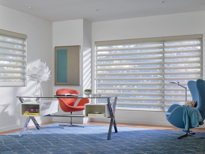 A home office with an orange desk chair and a blue side chair and rug.